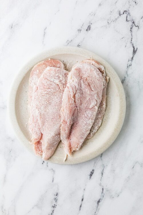 Raw chicken breasts on a marble surface, ready for cooking or baking.