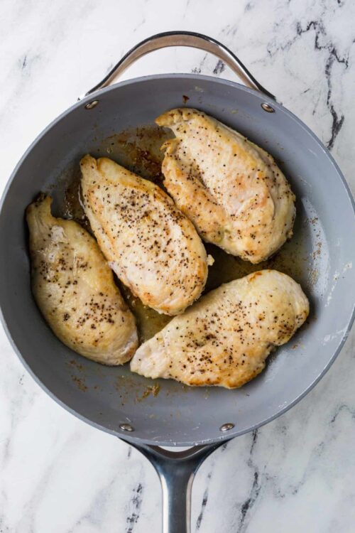 Juicy baked chicken breasts in a gray skillet with seasoning and melted butter.