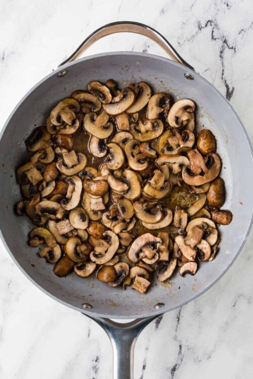 Sauteed sliced mushrooms in a gray skillet on white marble surface.