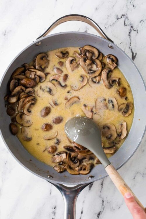 Creamy mushroom sauce cooking in a skillet with fresh sliced mushrooms, perfect for hearty recipes.