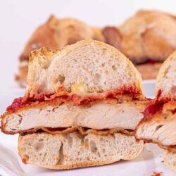 Buttered chicken sandwich with crispy breading and melted cheese on a white plate.