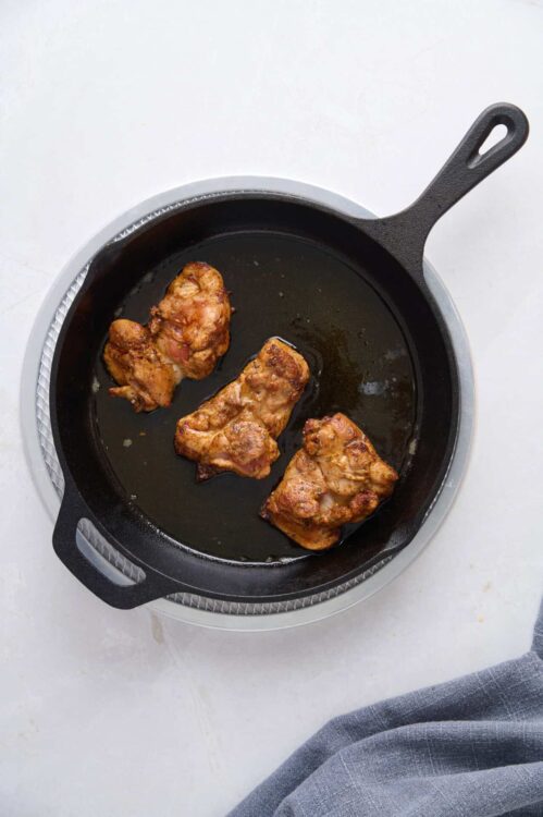 Juicy, crispy chicken thighs cooking in a cast iron skillet on a stovetop.