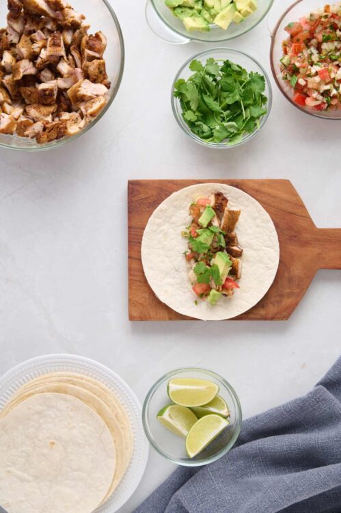Roma tomato, avocado, cilantro, chicken, and fresh ingredients for tacos.