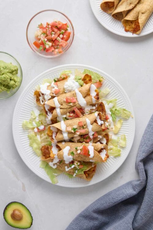 Crispy chicken tacos with fresh toppings drizzled with white sauce on a white plate.