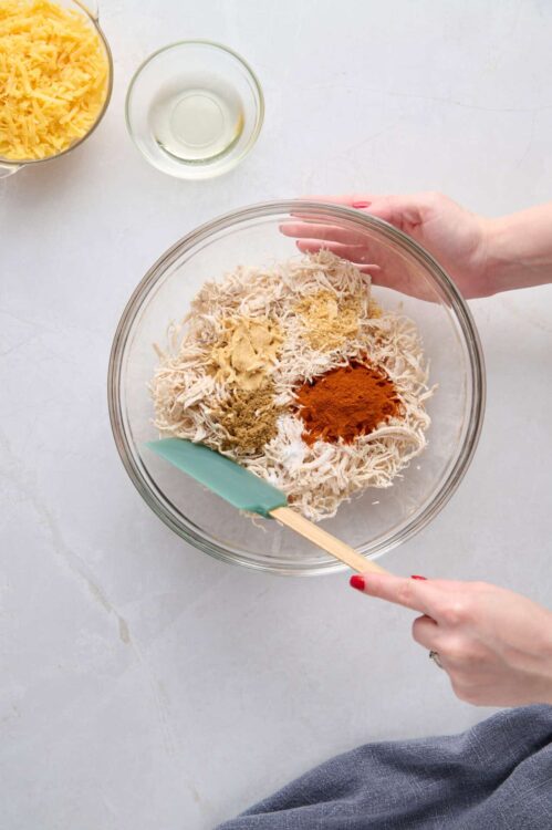 Cream cheese mixture with spices for baked cheese dip or spread, in a glass bowl on a white surface.