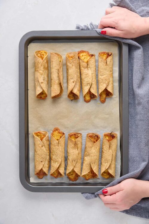 Golden breakfast enchiladas with crispy tortillas and melted cheese on baking sheet.