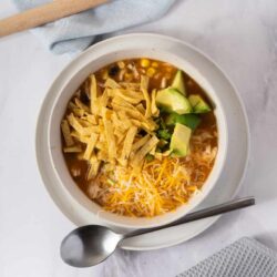 Creamy chicken tortilla soup topped with cheese, avocado, and crispy tortilla strips. Perfect cozy comfort food recipe.