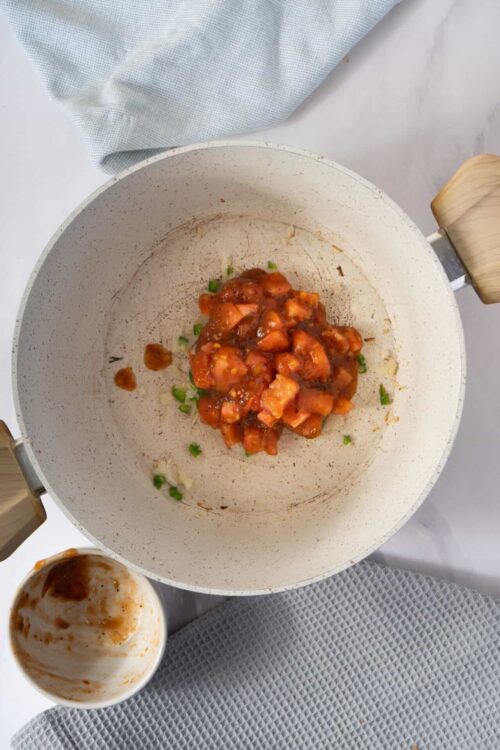 Sautéed chicken and green onions in a white skillet with cooking sauce.