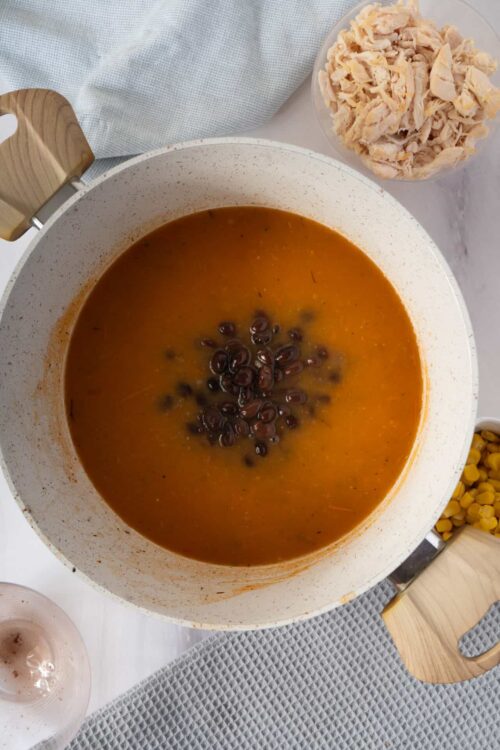 Creamy black bean soup with shredded chicken and corn, served in a white bowl on a light gray textured surface.