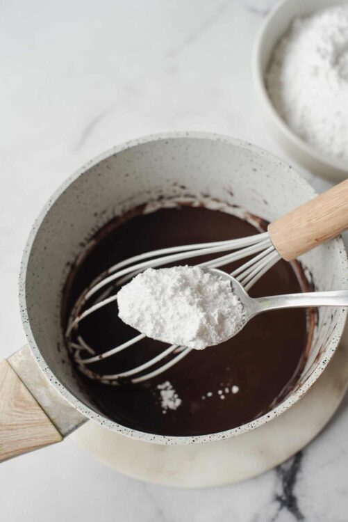 Creme de cacao being mixed with powdered sugar in a white mixing bowl.