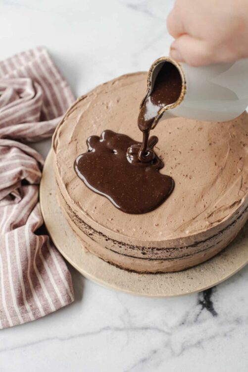 Rich chocolate frosting being spread on a layered cake, a spoon pouring warm chocolate ganache.