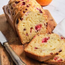 Fresh cranberry orange loaf cake with citrus and berry flavor, sliced on wooden serving board.