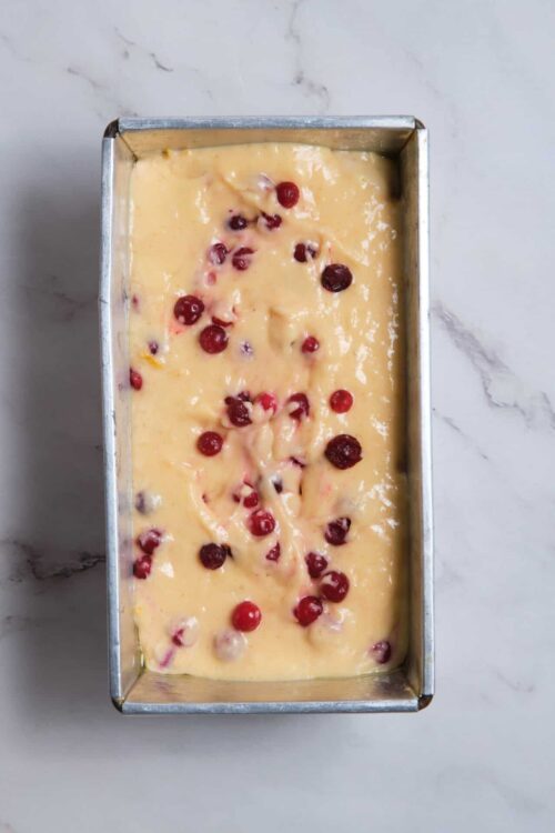 Fresh cranberry bread batter in a loaf pan with berries on top.