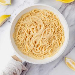 Buttered lemon garlic pasta in a white bowl on marble surface.
