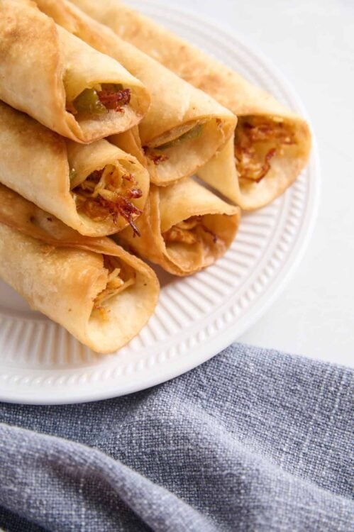 Crispy mini egg rolls stuffed with savory filling served on white plate.