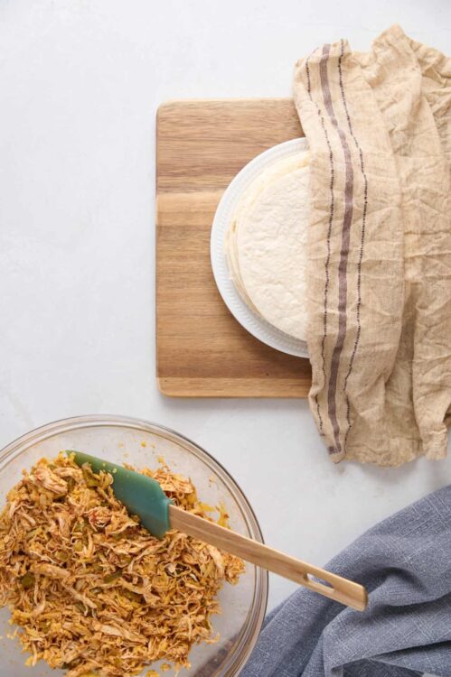 Shredded chicken mixture with vegetables in a glass bowl on a white countertop.