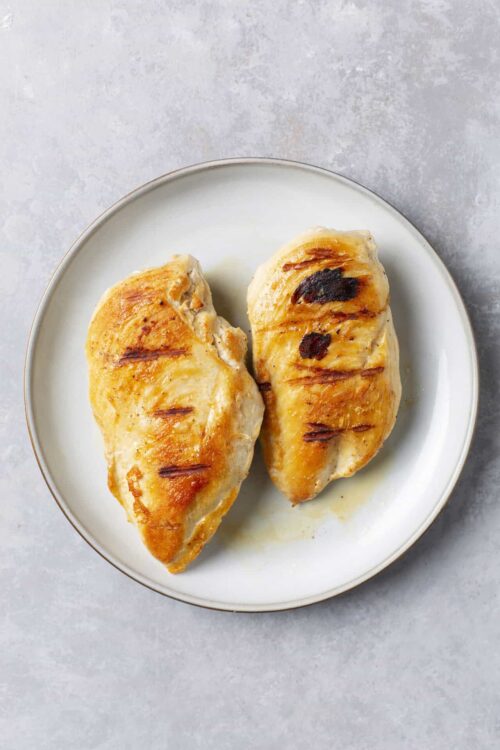 Baked chicken breasts with grill marks on white plate.