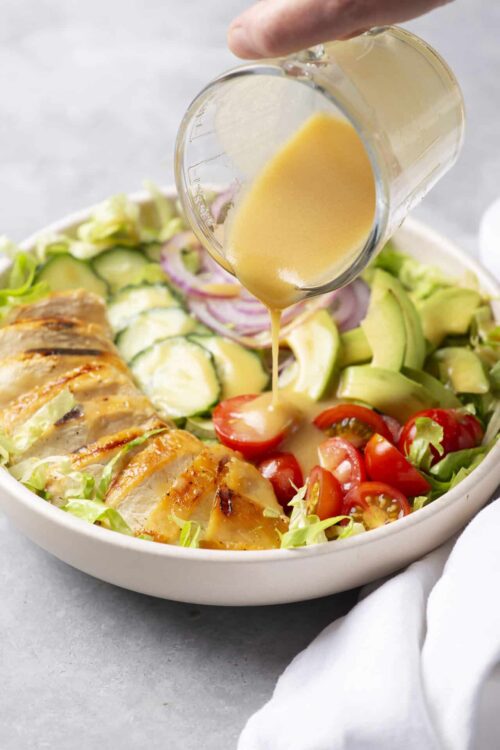 Fresh grilled chicken salad with homemade vinaigrette being poured over vibrant vegetables. Perfect for healthy meal options.