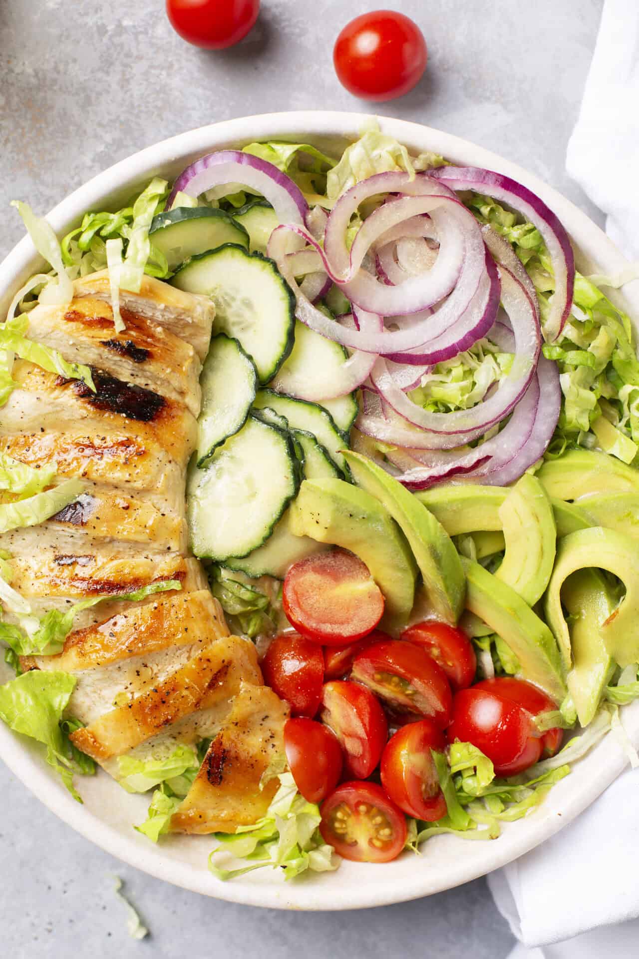 Fresh chicken salad with tomatoes, cucumbers, onions, and greens in a white bowl for healthy eating.