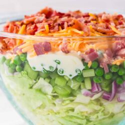 Fresh vegetable taco salad in a glass bowl with shredded cheese, bacon bits, and creamy ranch dressing.