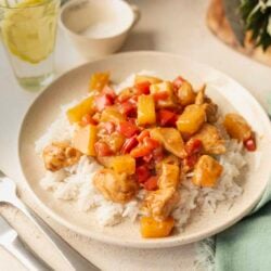 Savory chicken and pineapple stir-fry served over white rice in a beige bowl.