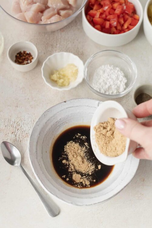 Savory marinade ingredients being prepared with soy sauce and brown sugar in a white mixing bowl.