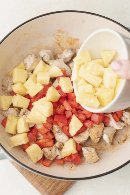 Diced pineapple, tomatoes, and cooked chicken being added to a skillet for a flavorful meal.