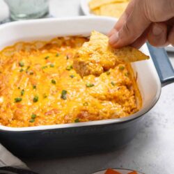 Baked cheesy dip in casserole dish with a chip being dipped in.