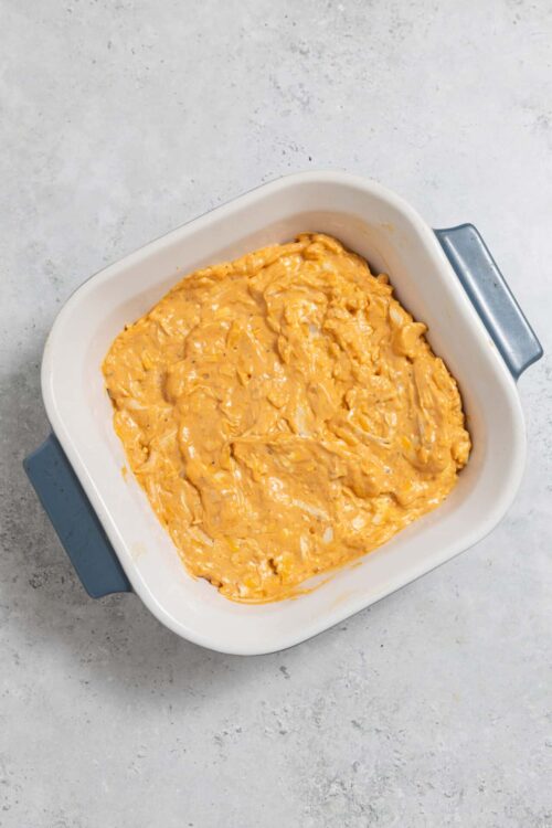 Creamy buffalo chicken dip in a white baking dish on a light gray surface.