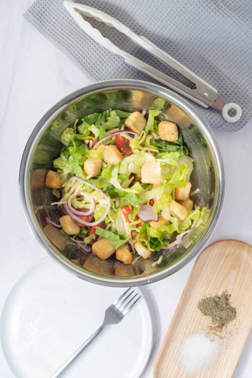 Fresh homemade Caesar salad in a stainless steel bowl with croutons, red onion, and cherry tomatoes. Perfect for a light, healthy meal or side dish.