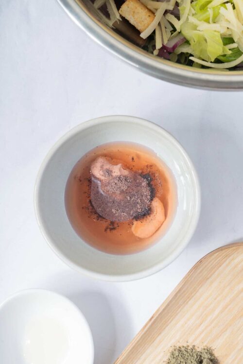 Botanical sea salt and pepper in a white bowl, with fresh chopped greens and croutons in a salad bowl.