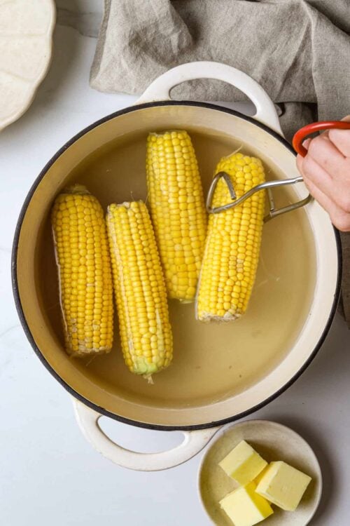 Boiled corn on the cob in a white pot, ready for butter and seasoning, showcasing easy corn cooking at Baked Bree.
