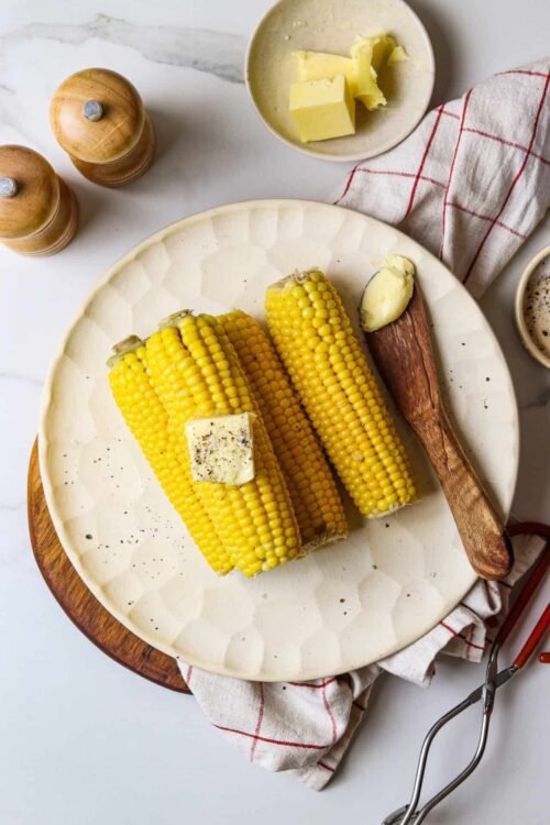 Golden corn on the cob with butter, ready to serve, on a white plate.