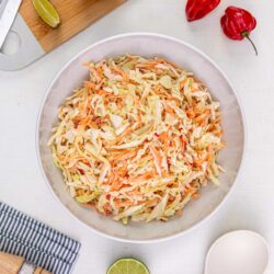 Cabbage slaw with carrots and lime wedges on white background, topped with sliced peppers.