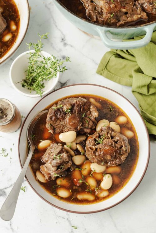 Slow cooker beef bourguignon with tender beef, white beans, and fresh thyme, served in a bowl on a white marble surface.