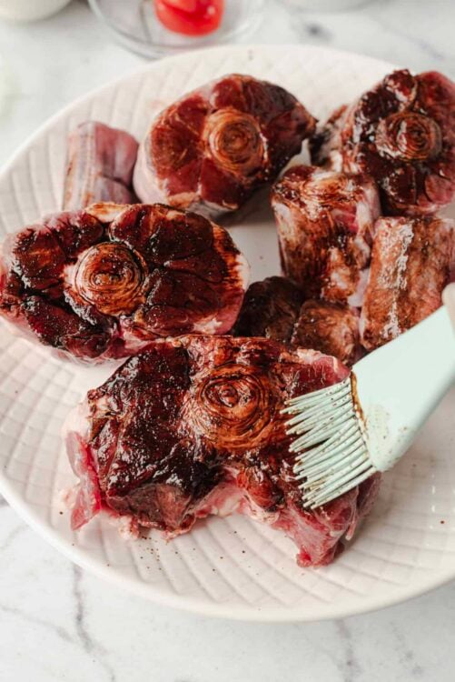 Fresh osso buco meat with marrow bones on a white plate, prepared for cooking or roasting.