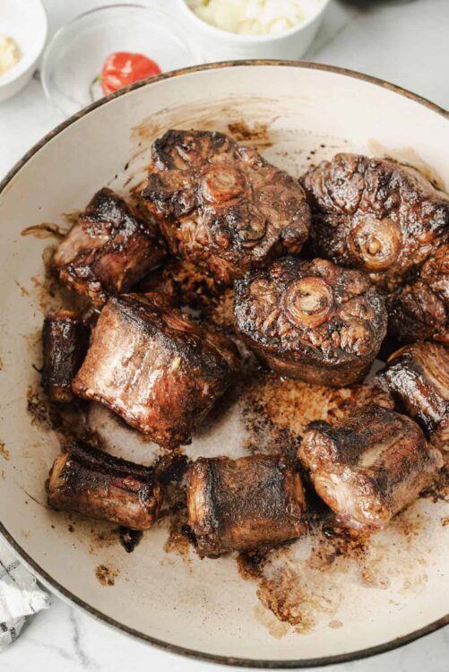 Succulent slow-cooked beef short ribs with caramelized exterior in a white skillet. Perfect for comforting family dinners and hearty meals.