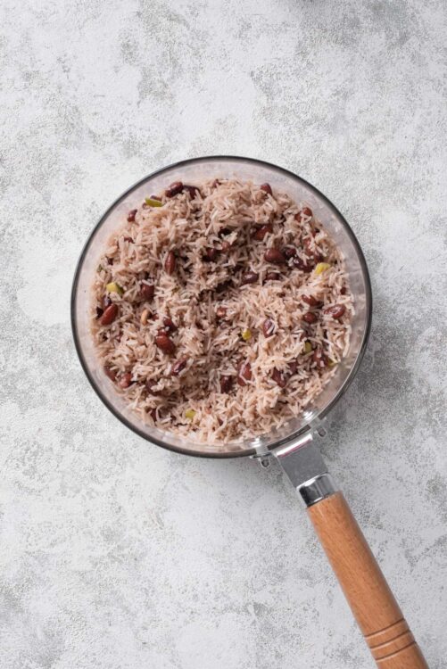 Fluffy cooked rice and kidney beans in a glass saucepan on a textured grey surface.
