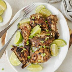 Savory grilled chicken drumsticks with lime and green onions on a white platter.