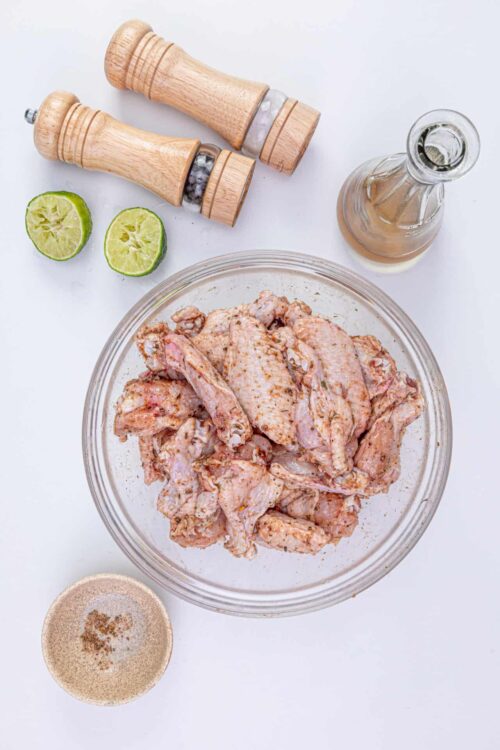 Marinated chicken pieces with lime, salt and pepper on white background.