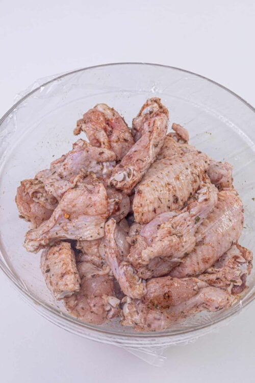 Seasoned raw chicken wings in a glass bowl, ready for cooking or baking.
