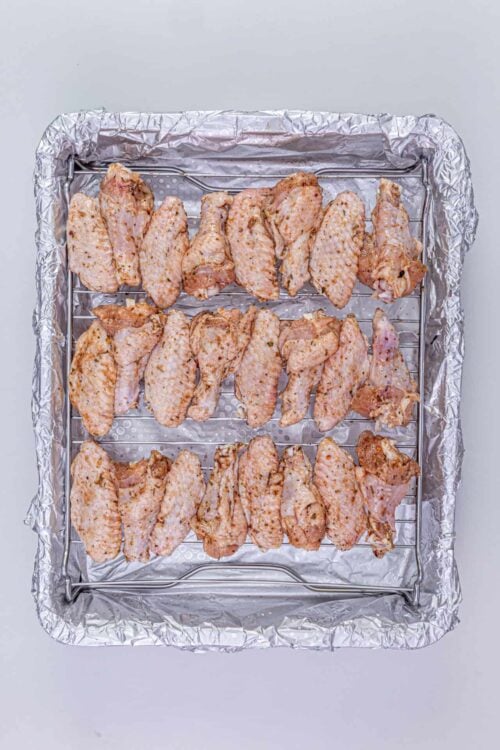 Juicy seasoned chicken wings on a baking rack lined with aluminum foil, ready for roasting or baking.