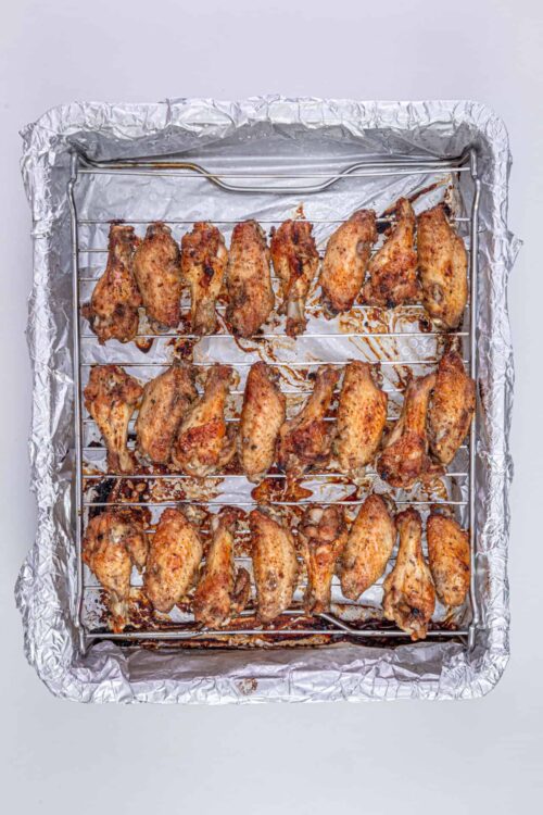 Crispy baked chicken wings on a wire rack lined with aluminum foil. Perfect for homemade chicken wing recipes and game day snacks.