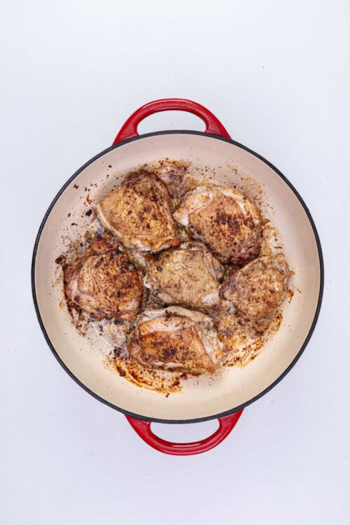 Juicy, golden-brown chicken thighs roasting in a red cast iron skillet.