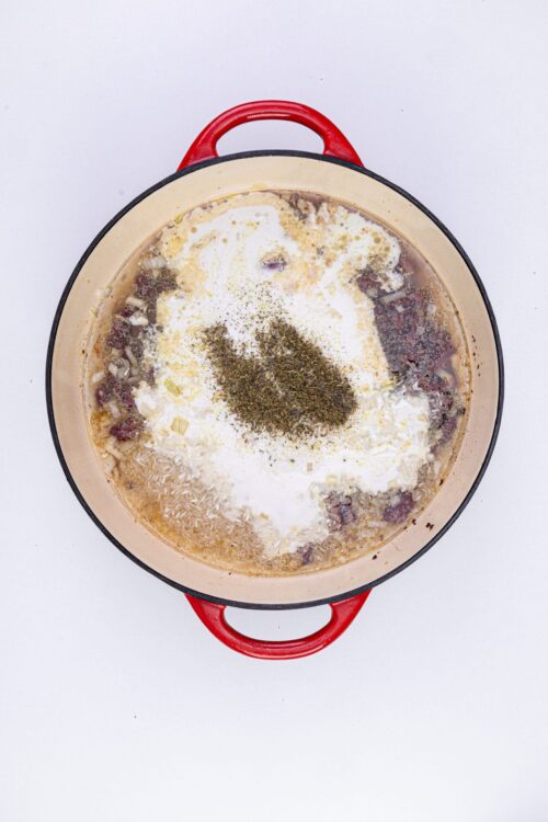 Creamy soup with herbs, rice, and ingredients in a red-rimmed pot.