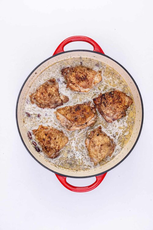 Golden brown pan-fried chicken thighs in creamy sauce, cooked in a red enamel skillet.