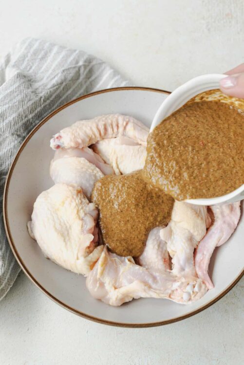 Buttermilk marinade poured over raw chicken wings in a white dish.