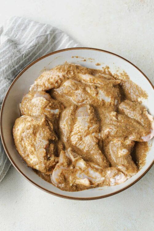 Juicy raw chicken thighs coated in seasoned marinade in a white bowl.
