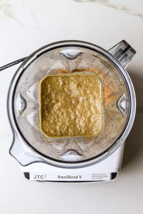 Creamy green pesto sauce blended in a glass blender on a white countertop, perfect for pasta or sandwiches.
