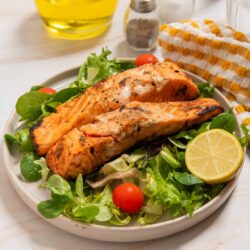 Grilled salmon fillets served on a fresh green salad with cherry tomatoes and lemon wedges.